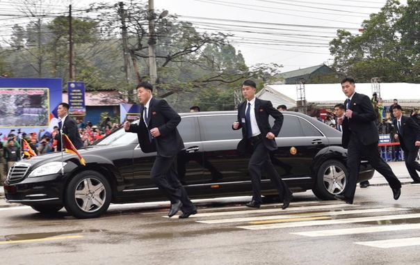 Ким Чен Ын во Вьетнаме едет на бронированном автомобиле, рядом с которым по периметру бегут охранники.